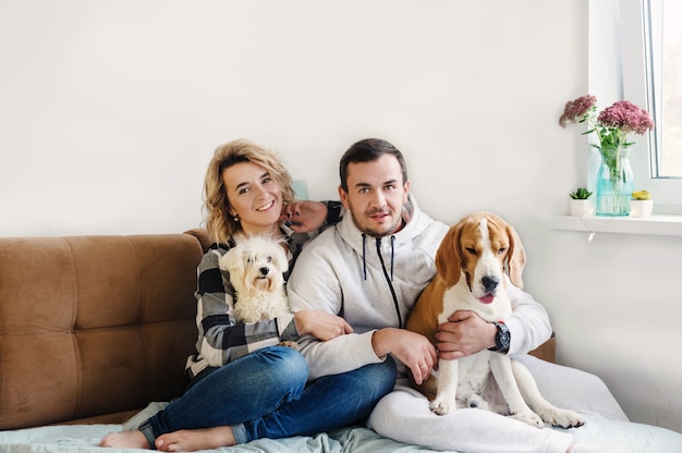 Happy young couple hugs two cute dogs sitting on the sofa