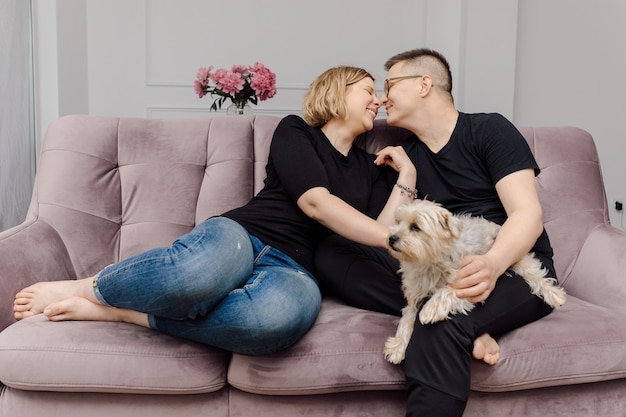 Happy young couple is havinggreat time on pink sofa in their\
living room pet yorkshire terrier.