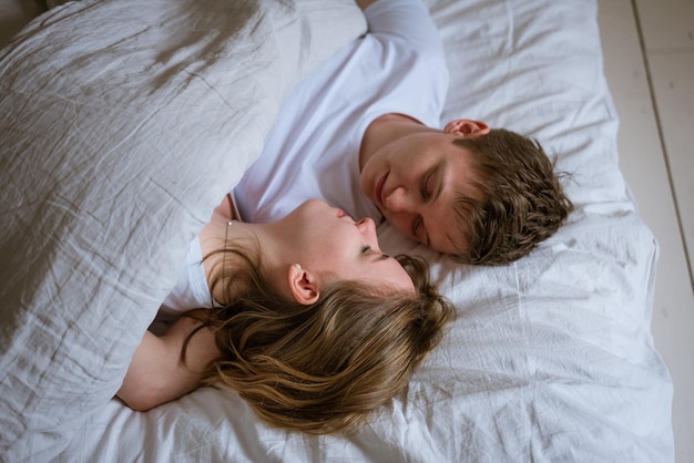 Happy young couple lie in bed and hug each other on white bed linen look