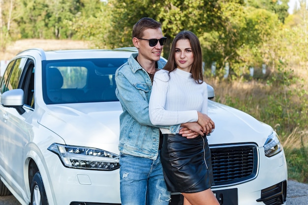 Happy young couple in love smiling and hugging near the white car.young couple hugs near the car