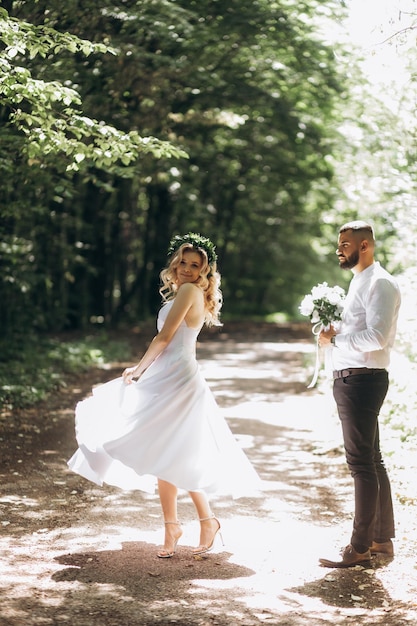 A happy young couple in love walk in a garden a man in a white\
shirt and a girl in a white light dress are walking in a park