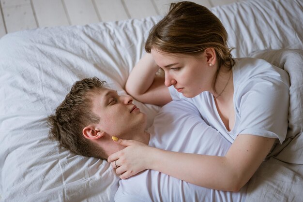 Happy young couple lying on bed smiling as they wake up in trendy hotel room