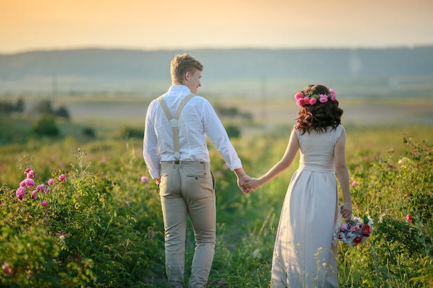 Счастливая молодая пара мужчина и женщина, взрослая романтическая семья. Встречайте закат на пшеничном поле. Счастливой улыбкой. Девушка в руках держит подарок, букет цветов, из роз.