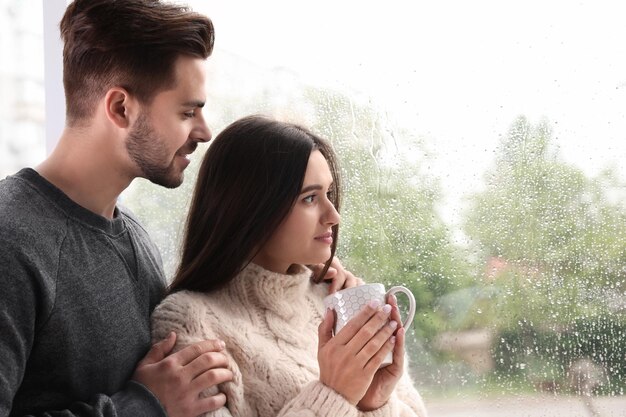 Happy young couple near window indoors on rainy day