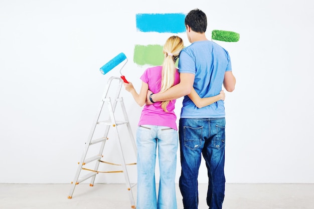 행복한 젊은 커플은 새 집의 녹색과 파란색 흰색 벽에 페인트를 칠합니다.