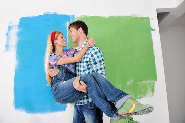 행복한 젊은 커플은 새 집의 녹색과 파란색 흰색 벽에 페인트를 칠합니다.