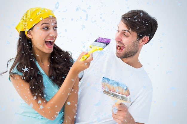 Happy young couple painting together and laughing against snow falling