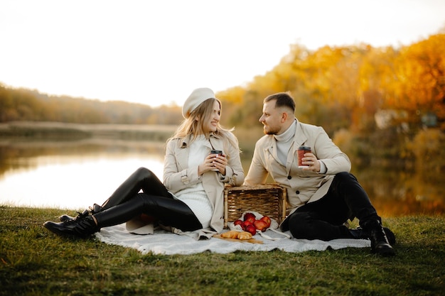 晴れた秋の日に屋外でピクニックをする幸せな若い夫婦、秋の公園の芝生の上に座る夫婦