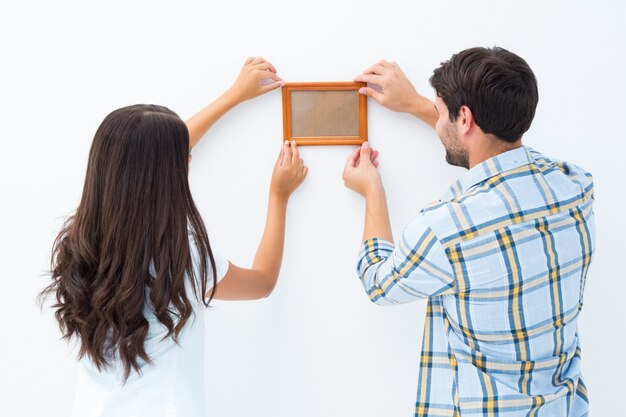 Happy young couple putting up picture frame on white background