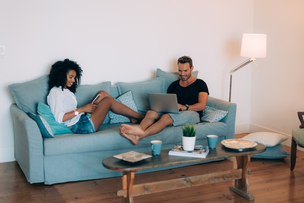 Happy young couple relaxed at home in the couch on the mobile phone and computer