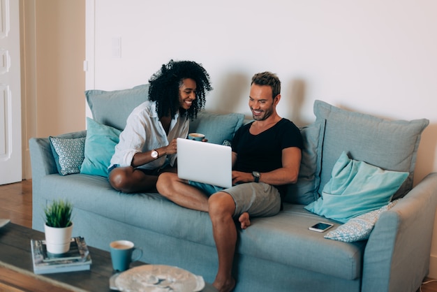 Happy young couple relaxed at home in the couch on the mobile phone and computer