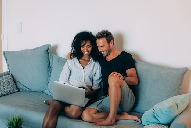 Happy young couple relaxed at home sitting in the couch on the computer