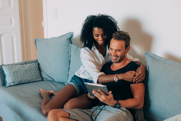 Happy young couple relaxed at home sitting in the couch on the tablet