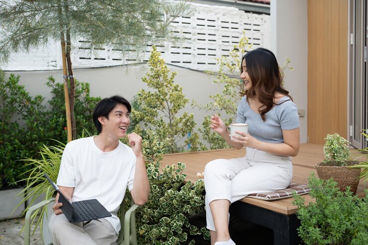 幸せな若い夫婦が裏庭でテクノロジーとコーヒーでリラックスしています