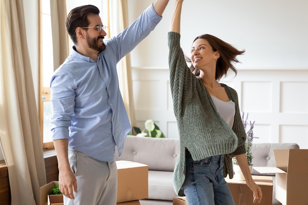 Happy young couple renters dance celebrate buying first house together Smiling Caucasian man and woman tenants have fun moving relocating to own new home Rental real estate tenancy concept