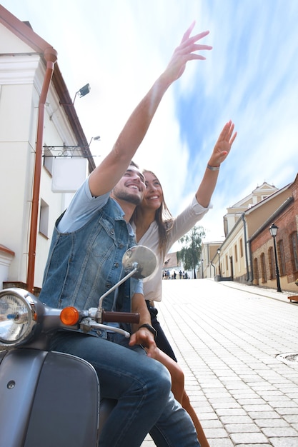 町でスクーターに乗って幸せな若いカップル。ハンサムな男と若い女性が旅行します。冒険と休暇の概念。