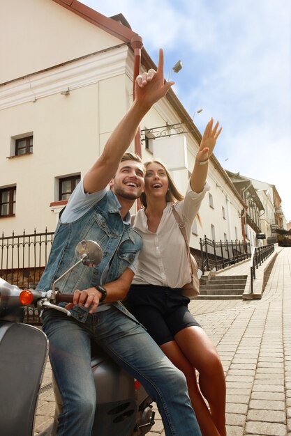 Happy young couple riding scooter in town. Handsome guy and young woman travel. Adventure and vacations concept.