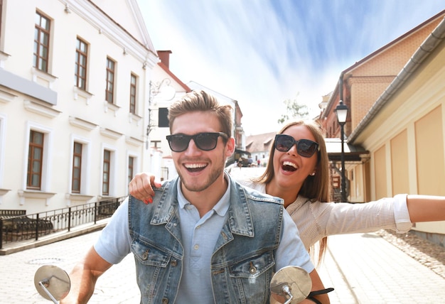 Happy young couple riding scooter in town. Handsome guy and young woman travel. Adventure and vacations concept.