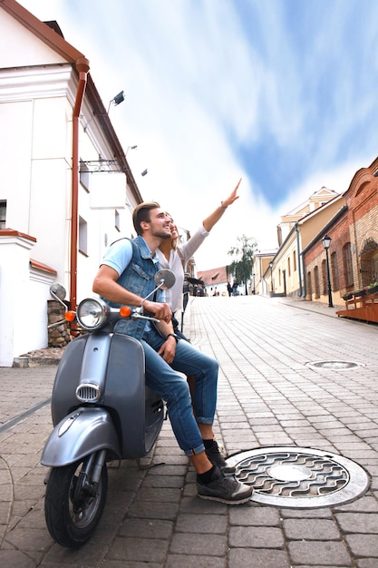 町でスクーターに乗って幸せな若いカップル。ハンサムな男と若い女性が旅行します。冒険と休暇の概念。