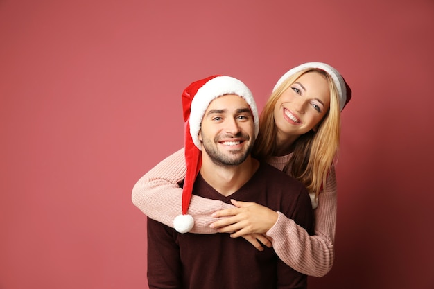 Happy young couple in Santa hats on color background. Christmas concept