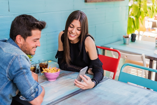 Disposizione dei posti a sedere felice delle giovani coppie in un ristorante con uno smartphone