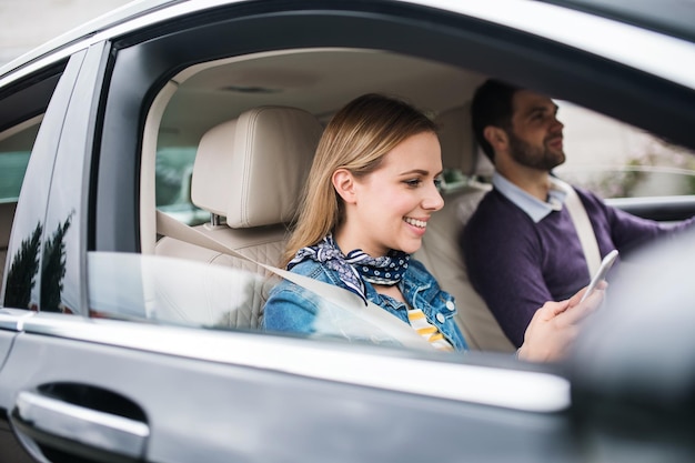 Happy young couple sitting in car using smartphone
