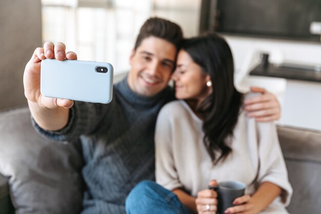 Happy young couple sitting on a couch at home, drinking tea