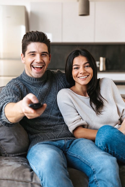 Happy young couple sitting on a couch at home, watching TV