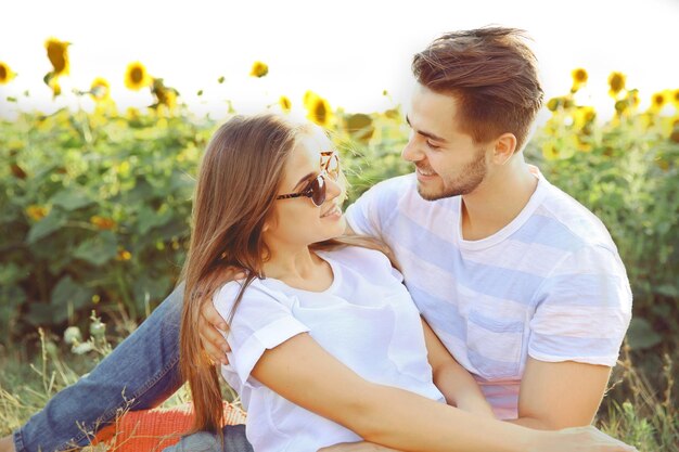 Happy young couple sitting in the field of sunflowers