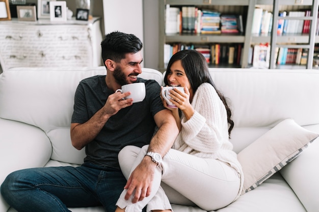 Happy young couple sitting on sofa holding white coffee cup