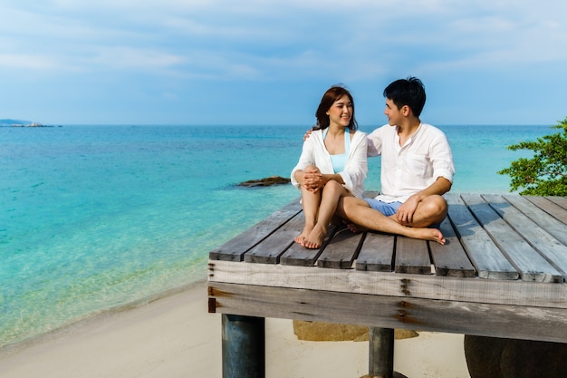 Happy young couple sitting on a wood bridge and sea beach at Koh MunNork Island, Rayong, Thailand