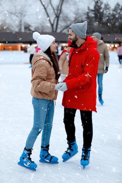 Photo happy young couple skating at outdoor ice rink