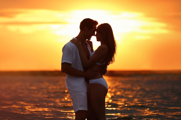 Happy young couple spending time together on sea beach at sunset