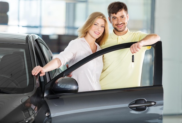 Photo happy, young couple standing by new car in showroom