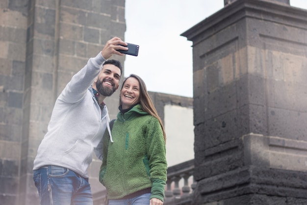 スペインのラスパルマス旧市街で冬の寒い日に携帯電話で自分撮りをしている幸せな若いカップル。