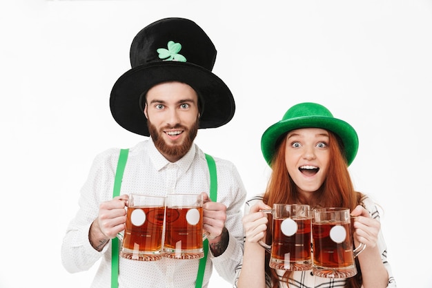 Happy young couple wearing costumes, celebrating StPatrick 's Day isolated over white wall, drinking beer