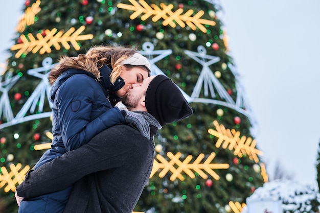 Happy young couple wearing warm clothes standing near a city Christmas tree, enjoying spending time together