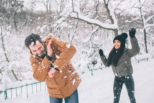 冬の幸せな若いカップル。家族のアウトドア。男と女が上向きに見て笑っています。愛、楽しさ、季節、そして人々-冬の公園を歩いています。彼は雪だるまです