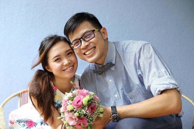 Happy young couple with bouquet of flowers on light background