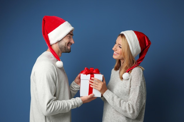 Счастливая молодая пара с рождественским подарком на цветном фоне