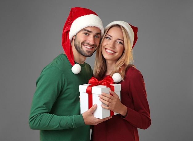 Happy young couple with Christmas present on grey surface