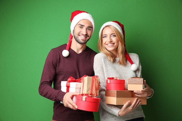 Happy young couple with Christmas presents on color background