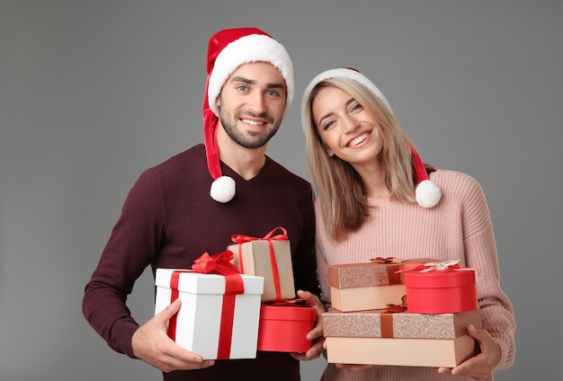 Happy young couple with Christmas presents on grey background