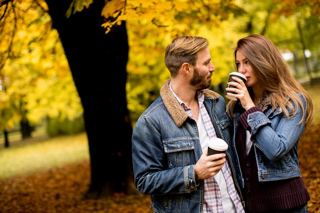 Happy young couple with coffee cups walking in autumn park