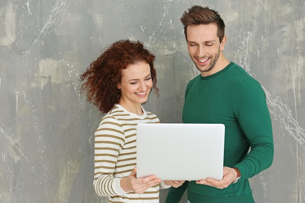 Happy young couple with laptop near grunge wall