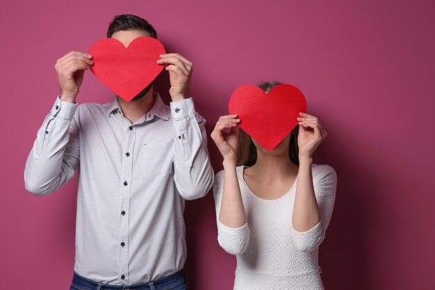 Happy young couple with red hearts on color background