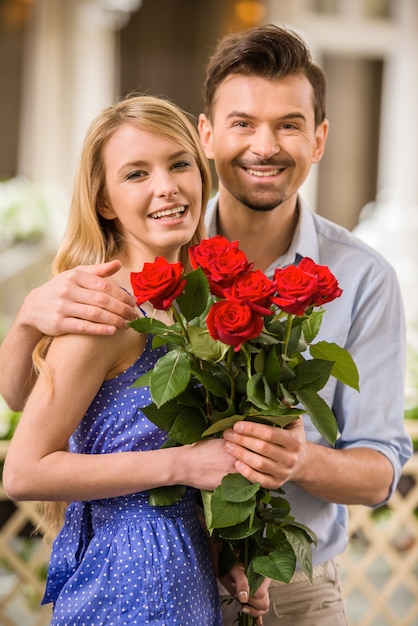 日にバラの花束と幸せな若いカップル。