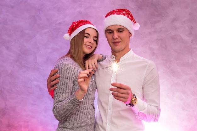 Счастливая молодая пара с Санта шляпу и Рождественские бенгальские огни студия стреляла.