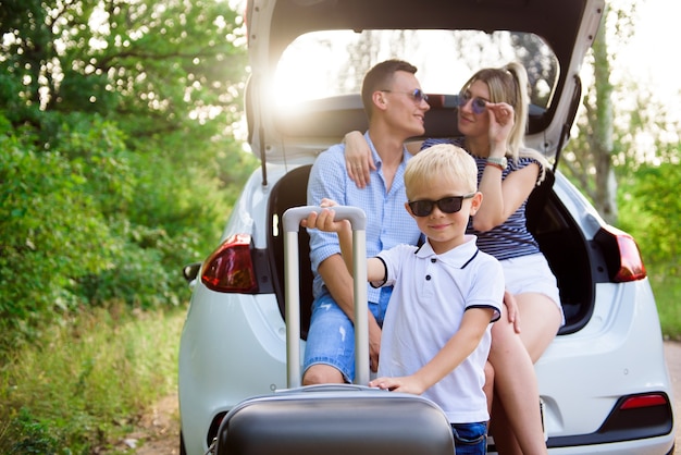 Happy young couple with son having a coffee break while traveling in the countryside. A man and a woman are sitting in the trunk of a car and rest.