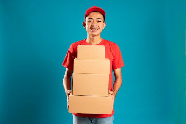 Счастливый молодой курьер держит картонную коробку и улыбается, стоя на синем фоне
